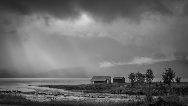 Gray clouds over a small cabin by the water.