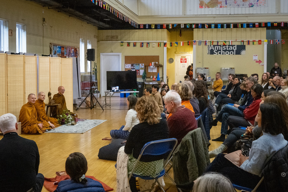 Three monks handling a Q&A in a people-filled gymnasium.