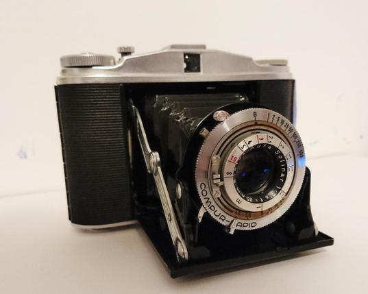 Farbfoto einer ausgeklappten Agfa Isolette II, einer von 1950 bis 1960 gebauten Faltkamera für Mittelformatfilm. Die hier gezeigte Variante hat ein Agfa Solinar-Objektiv und einen Compur-Rapid-Verschluss.