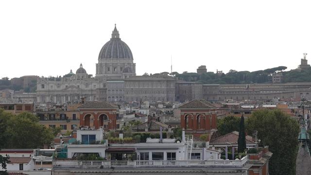 A distant view of the Vatican City and St. Peter's Basilica, seen from a promenade on the edge of the garden. The spot is popular with lots of people taking shots or admiring the view.
