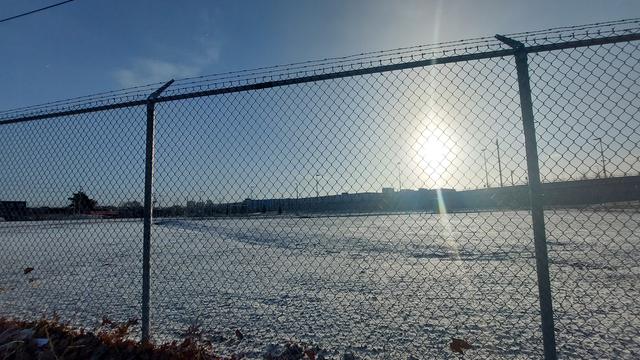 Early morning in an industrial area of Toronto. The sun is up, but low in the sky over a fenced-in field.