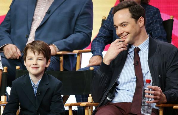 A photograph of two actors -- one who plays "Young Sheldon" (Shelly Cooper), and the other who plays adult Sheldon Cooper on the Big Bang Theory. They are both wearing blue checkered shirts and dark blue suit jackets and are smiling.