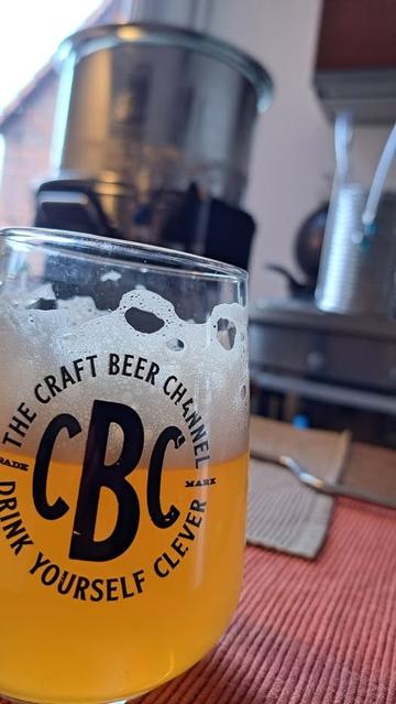 Im Vordergrund ein Glas mit Bier aus eigener Produktion. Im Hintergrund ist verschwommen der Braukessel zu sehen, aus dem der Treberkorb herausgenommen wurde. Situationsbild für den Begriff Läuterruhe