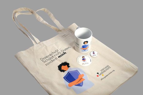 Das Foto zeigt Merch-Produkte der Stiftung Datenschutz: einen Beutel, eine Tasse, einen Sticker und ein Magnet mit dem Aufdruck "Datenschutz - schützt nicht Daten, sondern mich!"