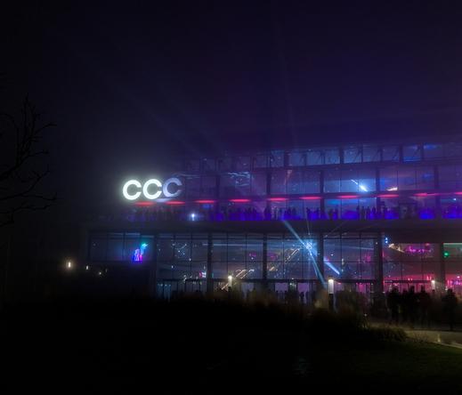 The new CCH building at night, with the huge glass hall. in a dim blue and red lighting. The CCH logo has been modified to say "CCC". There is a shiny bretzel in the middle of the hall reflecting light rays. A multicolored unicorn can be seen under the CCC logo.