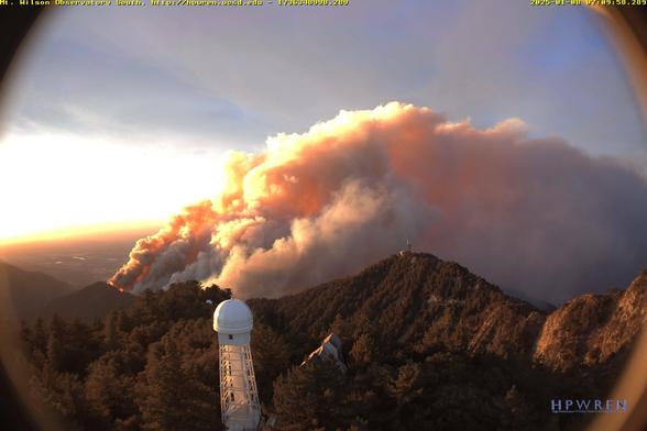 Fisheye image showing a Mount Wilson solar observatory tower in the foreground, sitting in a forest, with a huge cloud of sunrise-lit firesmoke obscuring the view of Greater Los Angeles.