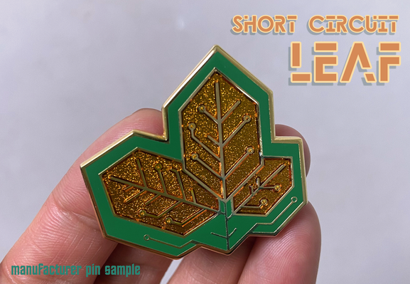 Handing holding a hybrid enamel pin of leaves designed to look like a printed circuit board (PCB) in green and gold.