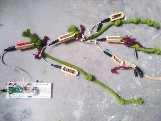 A network of small circuits inside wooden housings, some with coloured rope tied to them with patterns of knots indicating their ID. The tree structure is connected to a Raspberry Pi pico microcontroller with a small 8x8 LED screen that is showing a diagram representing the same hierarchical structure - which is able to be automatically read.