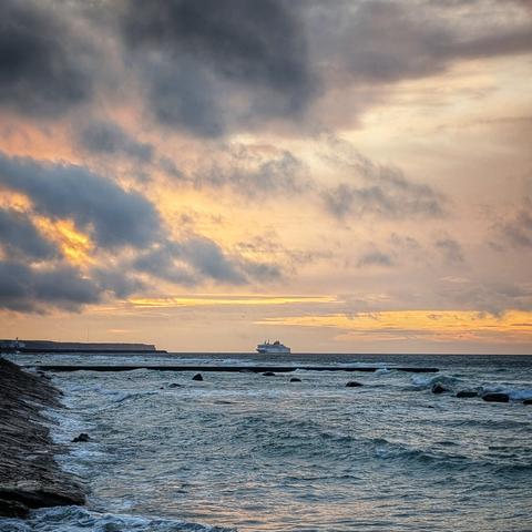 A passenger ferry arrives across the horizon as an early sunset breaks the grey clouds.