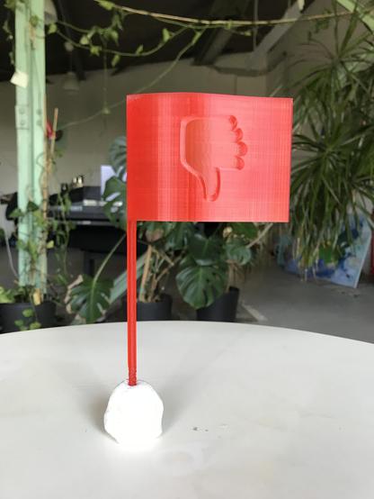 Ein rotes Fähnchen aus Plastik (aus dem 3D-Drucker), mit einem eingestanzten Daumen nach unten