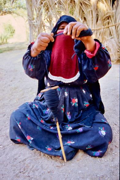 Vertical image of a bedouin woman, sit on the ground cross legged, spinning wool.