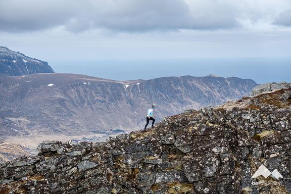Woman running up a mountain. Ocean in the background behind another mountain