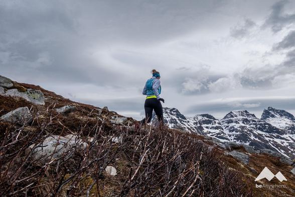 Woman running down from a mountain. Grey sky and some mountains with a bit of snow on top.