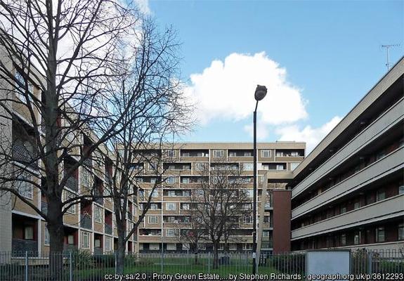 A photo of 1960s buildings, under a blue sky.  All the buildings are of concrete, with interest added by texturing rather than colour. On the left a 3 story range of housing, with inset balconies forming a chequerboard pattern. On the right a multi-storey car park, with exaggerated horizontal lines.  In the distance a 6-floor block of flats with patterned outlines.

The 3 frame and open green space, with trees (leafless in the winter) and an expanse of grass.
The atmosphere teeters between bleak and pleasant, leaving the viewer to decide.