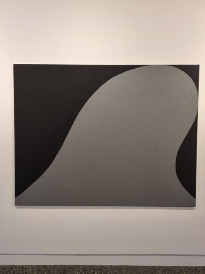 The first of a series of grey on black paintings by Matthew Harris depicting a sacred rock formation called Yeddonba near Wangaratta, titled "I know alone". Here, the formation is depicted as a single flat coloured silver semicircle shape that reaches towards the top left of the black canvas.