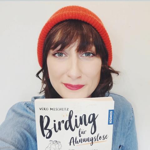 Véro mit roter Mütze, ihr Buch "Birding für Ahnungslose" haltend