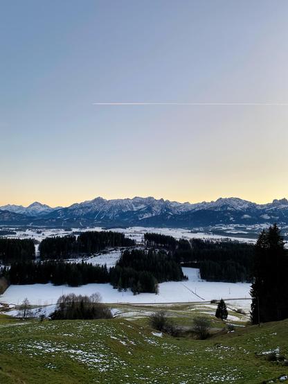 Serene sunset view from the hillside to an open snowy horizon of a clear sky with a mountain line in the distance, a small town at the foot.