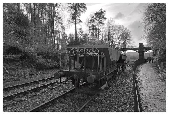 Black and white photograph showing railway hoppers on tracks alongside a public footpath.