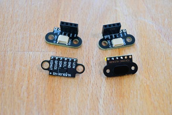 Two commercially available VL53L0X ToF (Time of Flight) sensor modules in front of two, small QWIIC (I2C) cable to header socket adapter PCBs allowing the ToF modules to easily plug into devices supporting QWIIC/STEMMA QT connectors.