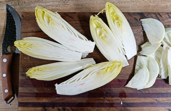 3 längs halbierte Chicorée und der geschnittene Fenchel auf einem Brett, neben dem Brett liegt ein Handliches Messer mit einer breiten, geschwungenen Klinge.