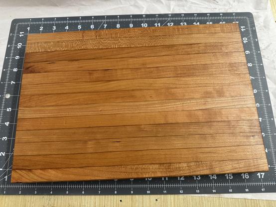 Image of a smooth wooden cutting board placed on a measurement mat with a ruler along the edges. The board has a rich, warm color and exhibits a fine grain pattern.