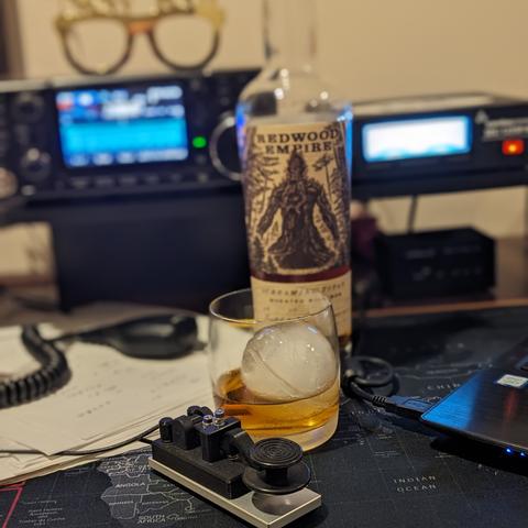 Photo of radio  with a Morse Code straight key and a bottle of bourbon in the foreground. The whiskey looks tasty