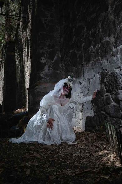 catrina in wedding dress kneeling by stone wall