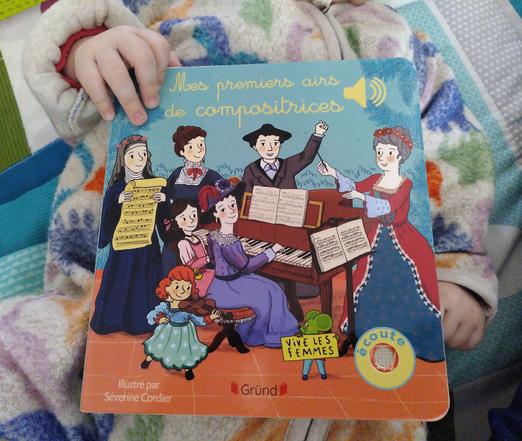 Livre musical "Mes premiers airs de compositrices" posé sur un bébé dont on aperçoit les mains