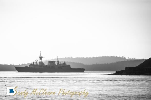 Warship underway partly in silhouette with an island behind.