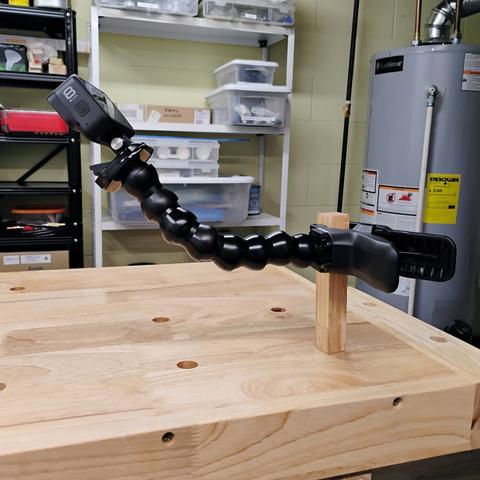 The top of my workbench is shown, with one of the dog pegs inserted.  My camera mount is clamped onto the peg, and my GoPro is attached to the other end of the mount, pointing down toward the workbench.

In the background you can see one of the walls of my shop.  There are two shelf units shown (one black and one white) with stuff stacked on the shelves, as well as the water heater.