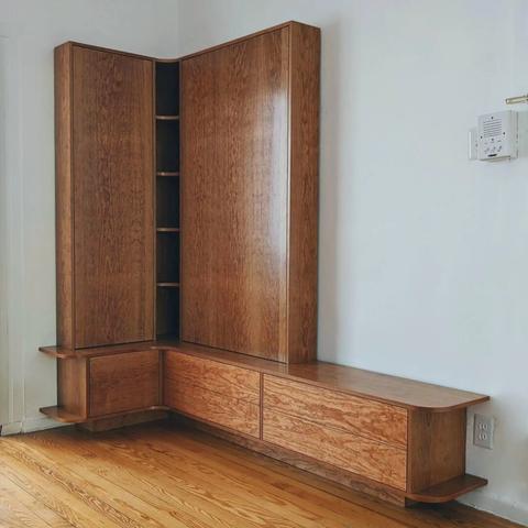 A custom cherry entryway bench and storage. The bench is an is a L shape and features 4 drawers and a small door. Above the bench are 2 large doors and a corner shelving unit.