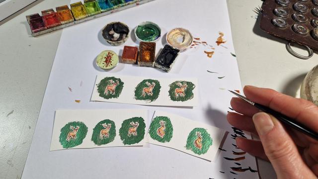 male mit Aquarellfarbe winzige Sika Hirsche (ca. 20-25mm jeweils) auf grünem Hintergrund