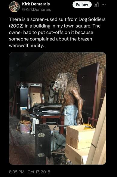 Tweet screenshot from @KirkDemarais Oct 17, 2018 

Text: "There is a screen-used suit from Dog Soldiers (2002) in a building in my town square. The owner had to put cut-offs on it because someone complained about the brazen werewolf nudity."

Picture shows a dim storeroom with various boxes and items. In the middle there is a Dog Solders werewolf suit apparently set up on a mannequin. It has a slim mostly hairless body, with a large hairy head. They are wearing bleached jean shorts.