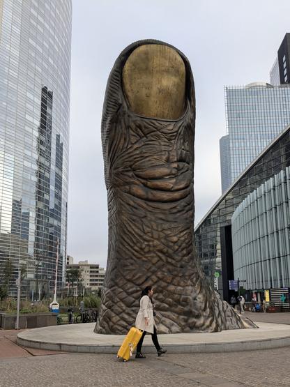 une femme avec une valise jaune passe devant le pouce de César à la défense