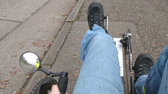 Rider's view on the KMX recumbent recumbent trike including rearview mirror. I'm wearing blue jeans and yellow hi-viz jacket (visible in mirror) and ankle safety straps.