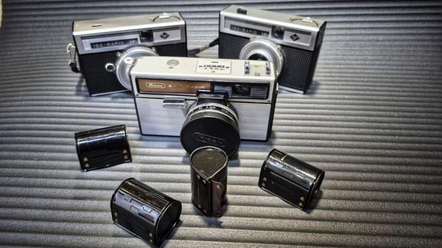 Three 1960s Rapid film system cameras. In front are four Rapid cassettes.