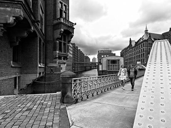 Hamburg – Speicherstadt two people walking on the iron bridge in the docks district of Hamburg. The photo in b/w with a cloudy incumbent sky