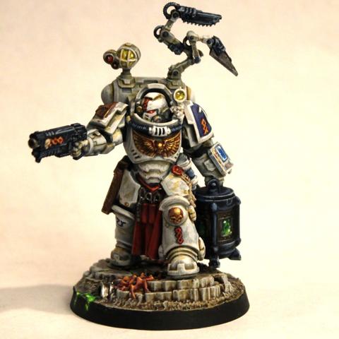Space Marine in white armor with gold wings on the chest. He holds a pistol in one hand and a blue-gray crate with a green glow coming from the windows into it. His armor has lights and vivisection tools on robotic arms and a tool-filled tabard down between his legs. He stands on grimy gray stones and dirt with weird growths and green ooze on it.