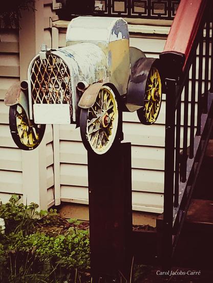 A mailbox shaped like a cream-colored old-fashioned car with a long bonnet and spoked wheels graces the banister next to the porch steps.