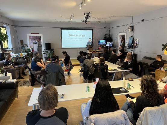 PVH at the front of a room full of people at tables in front of a slide with the logo for Ink & Switch