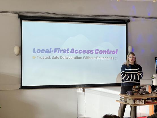 Woman in cool white glasses stands in front of a slide saying: Local-First Access Control: Trusted, Safe Collaboration Without Boundaries