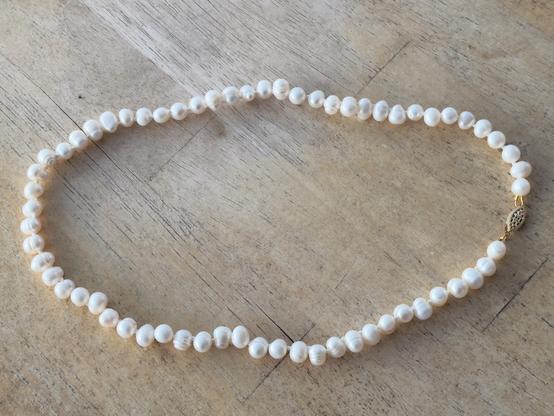A knotted pearl necklace with a gold clasp on a wood table