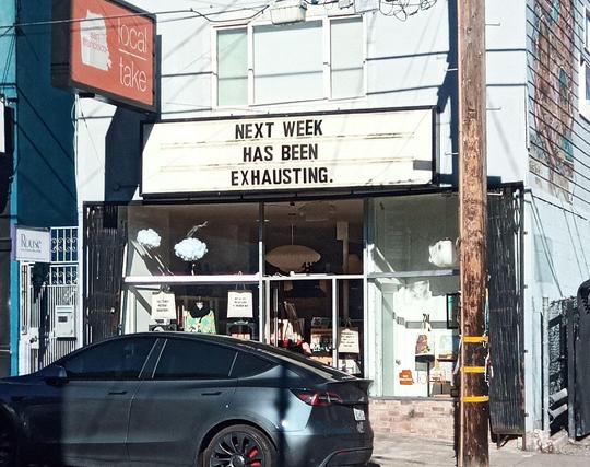 A store with a movie theater style marquee sign above the window. Across three lines it reads "Next week has been exhausting"