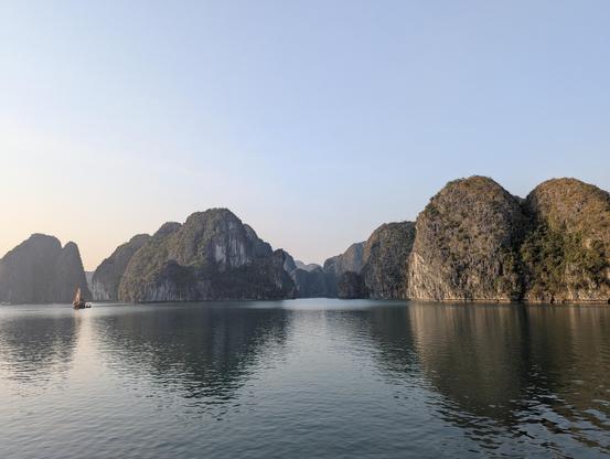 Limestone karsts rise majestically from the tranquil waters. A lone boat navigates the serene passage.