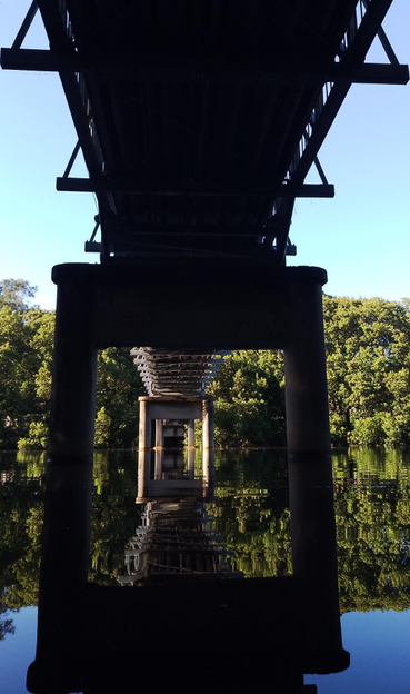 photo taken under a foot bridge looking across a river with the bridge reflected in the river.