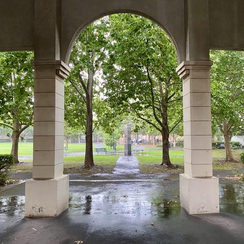 Looking out into Kensington’s Central Park through a faux neo-classical archway, into a leafy green scene in the rain
