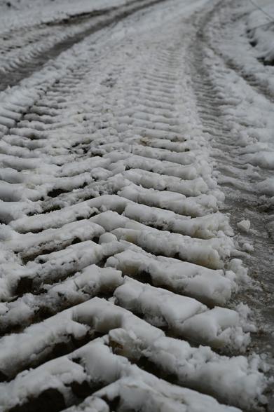Muster von schweren Traktorenreifen im Schnee. Der dreckige Feldweg kommt schon wieder zum Vorschein