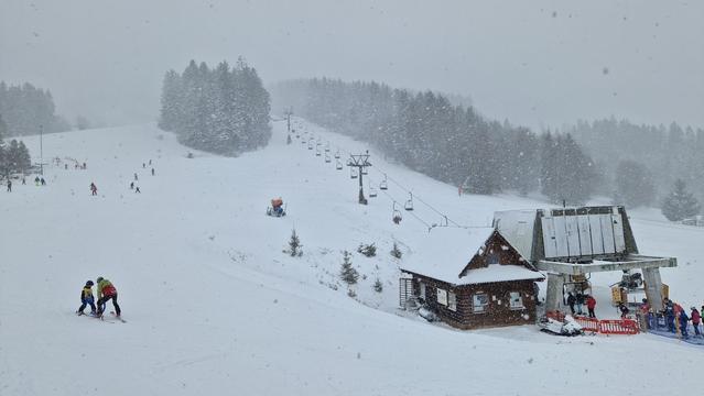 A view of snowy slopes with a lift. It's snowing.