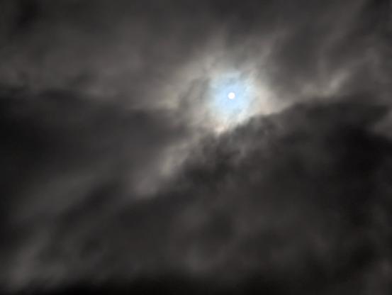 Written with the help of ChatGPT:

This image shows a close-up of the night sky. Dense, dark clouds dominate the scene, but leave an opening in their centre through which the waxing moon is visible. The moon appears as a bright point of light, its rays diffusely penetrating the clouds and gently illuminating them. The clouds appear dynamic, almost dramatic, and convey a mystical atmosphere. The combination of darkness, movement and the light of the moon creates a mysterious and slightly eerie atmosphere.