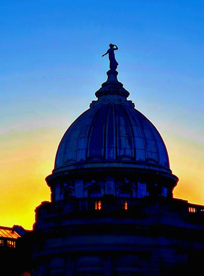 The dome of an Edwardian library topped with a female figure silhouetted against a sunset.